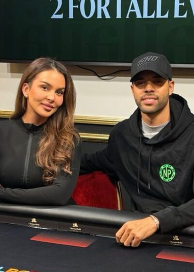 Nainen ja mies istuvat pokeripöydän ääressä, taustalla on televisio näyttö ja valkoista ja keltaista