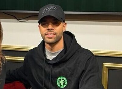 Nainen ja mies istuvat pokeripöydän ääressä, taustalla on televisio näyttö ja valkoista ja keltaista