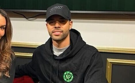 Nainen ja mies istuvat pokeripöydän ääressä, taustalla on televisio näyttö ja valkoista ja keltaista