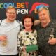 Kuvassa Ville Hakala perheineen seisoo rivissä äitinsä ja isänsä kanssa Coolbet Open plakaatin edessä. Äiti Päivi pitää kädessään vihreää laatikkoa.