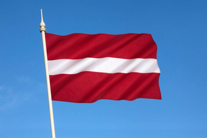 Kuvassa Latvian lippu, missä on punaista ja valkoista. Taustalla sininen taivas