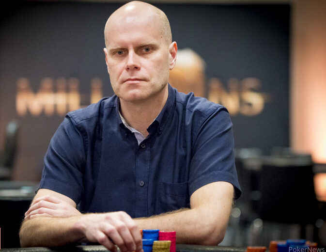 Kalju mies istuu sinisessä paidassa pokeripöydän ääressä. Hän on nimeltään Jari-Pekka Juhola. Taustalla lukee "Millions".
