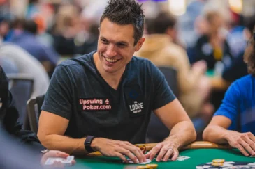 Doug Polk istuu vihreän pokeripöydän ääressä harmaassa T-paidassa ja pelimerkkejä ja pelikortteja edessään.