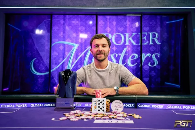Mies poseeraa pokeripöydän takana pokaalin kanssa. Edessä pöydällä on pelikortteja ja pelimerkkejä.