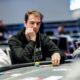Mietteliään näköinen mies istuu pokeripöydän ääressä ja nojaa käteensä. Miehellä on musta huppari ja nappikuulokkeet korvissa.