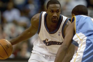 Koripalloilija. Miehellä on valkea koripallopaita ja hän on liikkeessä.