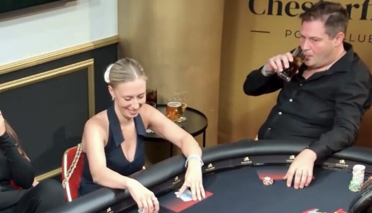 Mies ja nainen istuu pokeripöydässä. Miehellä on päällään musta kauluspaita ja hän juo lasista mustaa juotavaa. Nainen hymyilee.