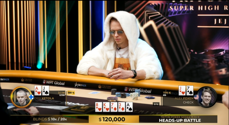 Mies istuu pokeripöydän äärellä valkoisessa hupparissa. Miehellä on päässään pyöreät auronkolasit ja edessään pelimerkkejä.