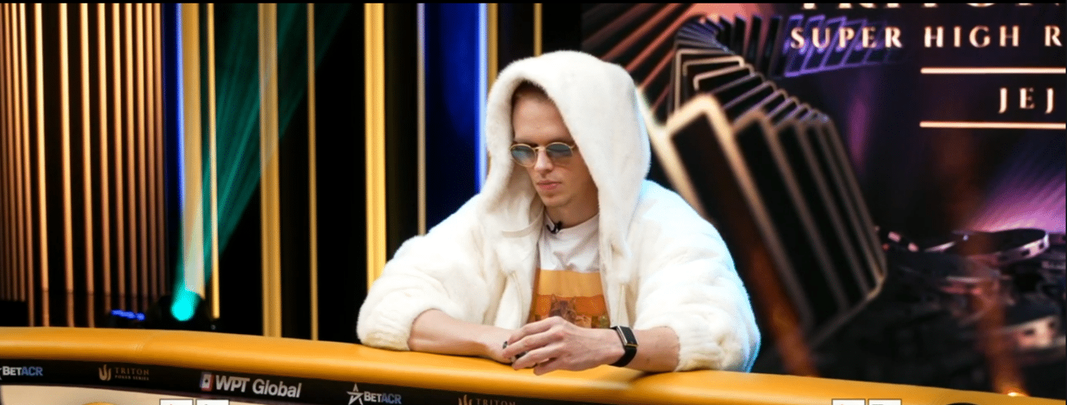 Mies istuu pokeripöydän äärellä valkoisessa hupparissa. Miehellä on päässään pyöreät auronkolasit ja edessään pelimerkkejä.