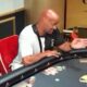 Jussi Helström pokeripöydän ääressä punaisella tuolilla kädet ojossa