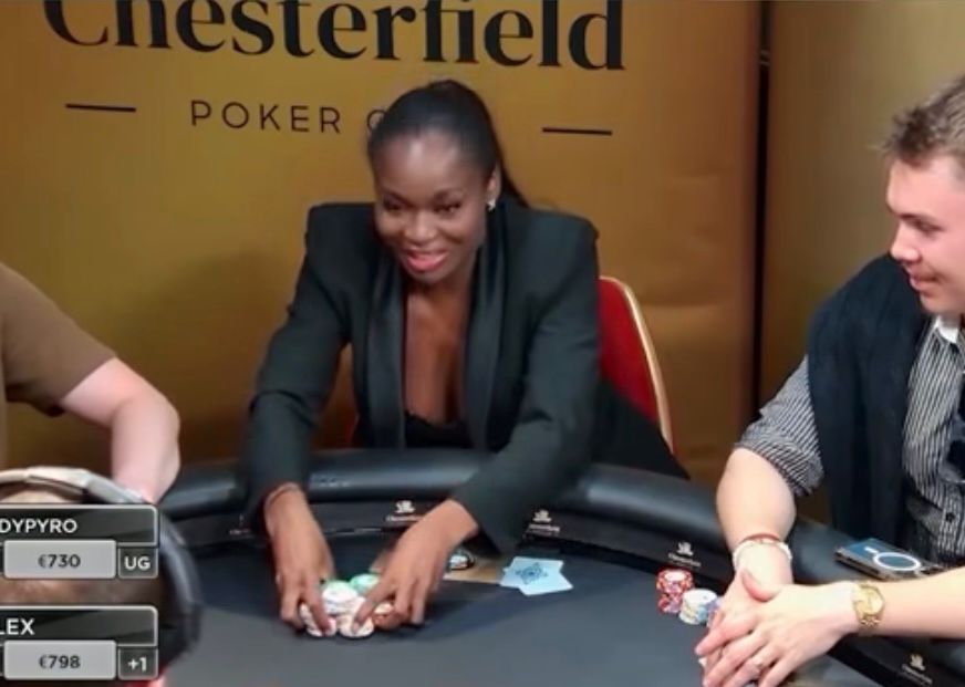 Kelly Kalonji istuu pokeripöydän ääressä musta jakkupuku päällä ja asettaa pelimerkkejä keskemmälle pöytää