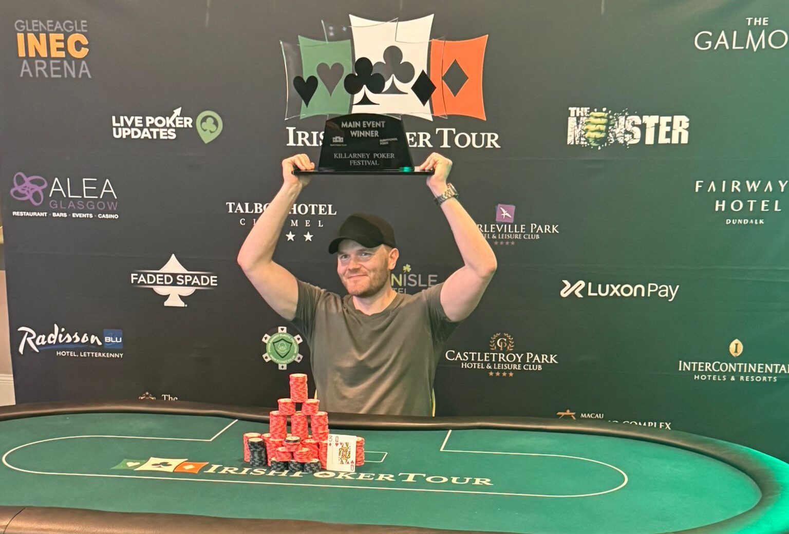 Samuel Saariaho istuu vihreän pokeripöydän ääressä pidellen Irish Open main eventin pyttyä päänsä päällä