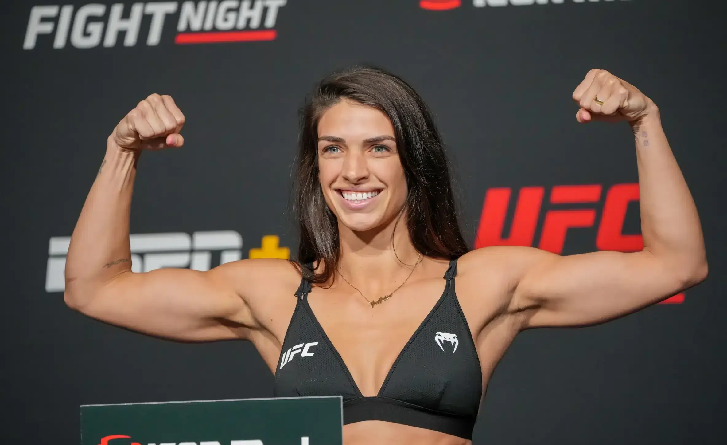 UFC-ottelija Mackenzie Dern näyttelee hauiksiaan UFC-valokuvausseinän edessä