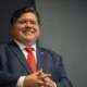 Illinoisin kuvernööri Pritzker sinisessä puvussa, punaisessa solmiossa, kädet ristittynä
