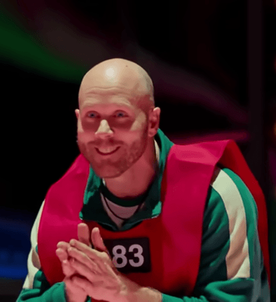 Steven Jones kisailee Squid Game -sarjassa päällään vihreä verkkapuku ja punainen liivi