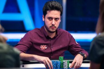 Adrian Mateos istuu pokeripöydässä. Hänellä on päällään punainen kauluspaita. Hänen kädet ovat pöydällä, jossa on myös pelimerkkejä.