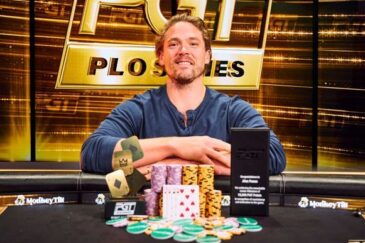 Alex Foxen istuu pokeripöydässä. Miehellä on päällään sininen paita, josta on hihat kääritty. Miehen edessä on pelimerkkejä ja kortteja.