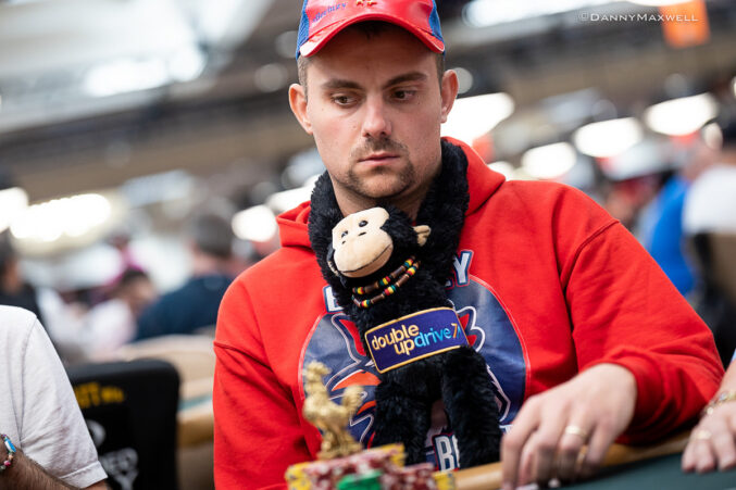 Kuvassa on pokeriturnaukseen osallistuva mies, jonka ilme on äärimmäisen keskittynyt. Hän istuu pelipöydän ääressä pukeutuneena punaiseen huppariin ja takaperin käännettyyn lippalakkiin. Huomion varastavat hänen persoonalliset onnenkalunsa: kaulan ympärille kiedottu musta pehmoapina sekä pelimerkkien edessä oleva pieni kultainen kukko-patsas. Pelaajan katse on tiukasti kiinnittynyt pöydän tapahtumiin. Valokuvaaja Danny Maxwell on onnistunut vangitsemaan hetken, jossa vakava keskittyminen yhdistyy leikkisään persoonallisuuteen.