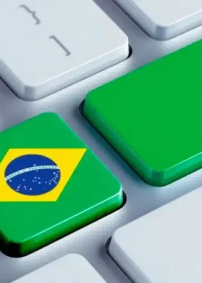 Kuvassa on tyylitelty lähikuva modernista tietokoneen näppäimistöstä. Kuva on sommitelma, joka kuvaa online-vedonlyöntiä Brasiliassa. Kaksi näppäintä on nostettu esiin: Enter-näppäin on korvattu suurella vihreällä näppäimellä, jossa lukee sana "bet" (lyö vetoa). Heti sen vieressä on näppäin, johon on kuvattu Brasilian lippu. Yksinkertainen mutta tehokas visuaalinen sommittelu viestii selkeästi brasilialaisille suunnatuista tai Brasiliassa tapahtuvasta nettipelaamisesta ja -vedonlyönnistä. Se on tyypillinen kuvituskuva, jota käytetään aiheeseen liittyvissä uutisissa ja artikkeleissa.