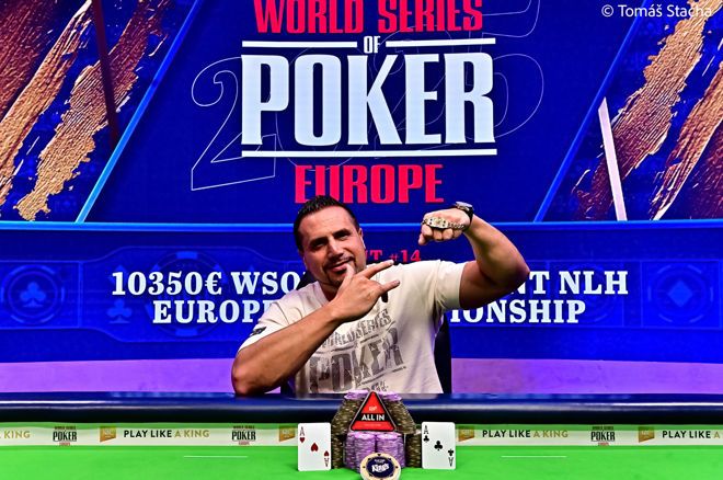 Kuvassa on pokerinpelaaja, joka juhlii suurta turnausvoittoaan World Series of Poker Europe (WSOPE) -tapahtumassa. Taustan sininen mainosseinä vahvistaa tapahtuman arvokkuuden. Voittaja poseeraa erittäin itsevarmana ja iloisena. Hän osoittaa toisella kädellään ranteessaan olevaa arvokasta ja haluttua WSOP-voittoranneketta, joka on pokerimaailman merkittävimpiä palkintoja. Hänen edessään pöydällä on suuri pino purppuranvärisiä pelimerkkejä, ja niiden molemmin puolin on esillä hänen voittokätensä: kaksi ässää. Kuva on täynnä energiaa ja vangitsee täydellisesti hetken, jolloin pelaaja on saavuttanut uransa huipun. Valokuvan on ottanut Tomáš Stacha.