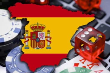 Kuvassa on digitaalinen sommitelma, joka kuvaa online-rahapelaamista Espanjassa. Kuvan keskeisenä elementtinä on Espanjan kartan muotoinen kuvio, joka on täytetty maan lipun väreillä ja vaakunalla. Tämä on asetettu kannettavan tietokoneen näppäimistön päälle, mikä symboloi internetiä ja verkkoympäristöä. Ympärillä on uhkapelaamiseen liittyviä esineitä, kuten pokerimerkkejä, läpikuultava punainen noppa ja pelikortteja (ässä ja kuningas). Kokonaisuus on tyypillinen kuvituskuva, joka viestii tehokkaasti Espanjan online-pelimarkkinoista, lainsäädännöstä tai maan pelikulttuurista.