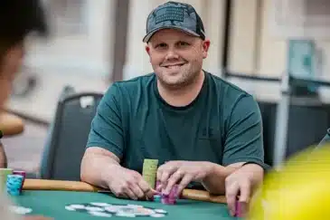 Hän istuu vihreän pelipöydän ääressä ja hymyilee lämpimästi kameralle. Hänellä on yllään tumma t-paita ja maastokuvioinen lippalakki, jonka etuosassa on Yhdysvaltain lippu -aiheinen merkki. Berryn edessä on suuria pinoja erivärisiä pelimerkkejä, ja hänen kätensä lepäävät niiden päällä. Tausta on sumennettu turnaussalille tyypilliseen tapaan. Kuva onnistuu vangitsemaan rennon ja itsevarman hetken keskeltä kovatasoista turnausta.