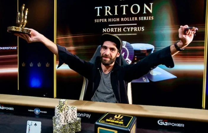 Kuvassa on ranskalainen pokerinpelaaja Grégoire Auzoux, joka juhlii riemukkaasti voittoaan suuressa pokeriturnauksessa. Hän istuu pelipöydän ääressä kädet voitonmerkiksi kohotettuina, pitäen toisessa kädessään näyttävää kultaista pokaalia. Hänen ilmeensä on täynnä aitoa iloa ja ylpeyttä. Taustalla oleva näyttö paljastaa tapahtuman: "TRITON SUPER HIGH ROLLER SERIES NORTH CYPRUS". Pöydällä Auzoux'n edessä on korkea pino pelimerkkejä, voittokortit sekä toinen palkintoesine. Kuva vangitsee täydellisesti uran merkittävän voitonhuuman hetken.