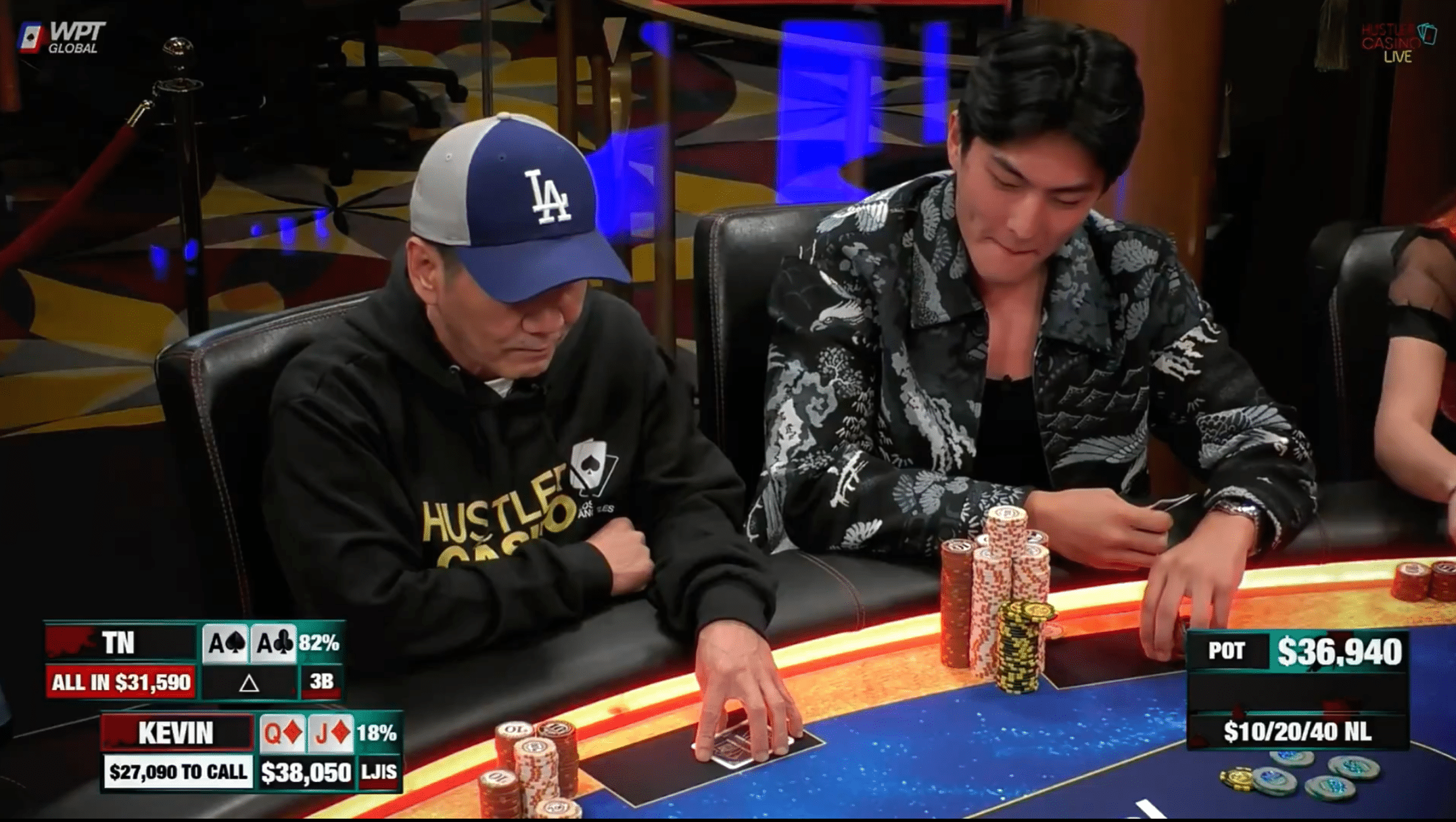 Tämä ruutukaappaus vangitsee erittäin jännittyneen hetken Hustler Casino Live -pokerilähetyksestä. Kaksi miestä istuu kirkkaasti valaistun pokeripöydän ääressä, ja panokset ovat korkeat. Vasemmalla istuva pelaaja, "Kevin", pukeutuneena LA-lippikseen ja Hustler Casino -huppariin, tuijottaa korttejaan syvissä mietteissään. Kuvan grafiikka paljastaa katsojille tilanteen: Kevinillä on kuningatar-jätkä-suited, mutta hän on vastustajan "TN":n all-in-panostuksen edessä, jolla on 92% voittosuosikki, taskuässät. Nuorempi, kuviopaitainen pelaaja oikealla seuraa tilannetta, kun potti on kasvanut jo lähes 37 000 dollariin.
