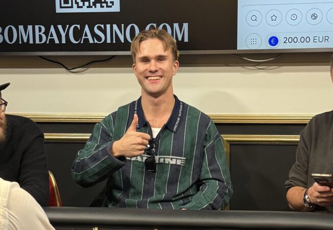 Joni "Stagala" Takala istuu pokeripöydässä kruunu päässään ja hymyilee kameralla peukaloa näyttäen.