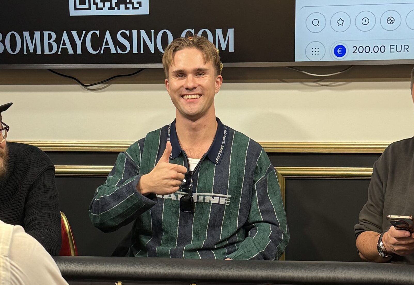 Joni "Stagala" Takala istuu pokeripöydässä kruunu päässään ja hymyilee kameralla peukaloa näyttäen.