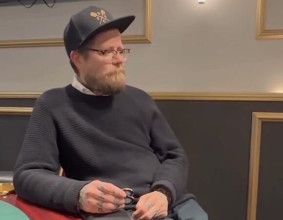 Wallu Valpio istuu pokeripöydässä. Hänellä on päässään tumma lippalakki ja tumma paita. Kädessään hänellä pari mustaa pelimerkkiä.