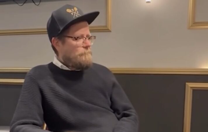 Wallu Valpio istuu pokeripöydässä. Hänellä on päässään tumma lippalakki ja tumma paita. Kädessään hänellä pari mustaa pelimerkkiä.