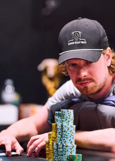 Joni Jouhkimainen istuu pokeripöydässä kasvoillaan tiukka ilme. Hänellä on päässään musta lippis ja edessään pelimerkkejä.