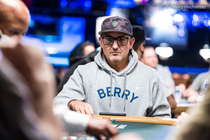 Kuvassa on yhdysvaltalainen huipputason pokeriammattilainen Josh Arieh. Hän on moninkertainen World Series of Poker (WSOP) -rannekkeen voittaja ja ansaitsi arvostetun WSOP Player of the Year -tittelin vuonna 2021. Kuvassa Arieh istuu pokeripöydässä äärimmäisen keskittyneenä ja tuijottaa intensiivisesti eteensä. Hänellä on yllään harmaa "BERRY"-huppari, silmälasit ja takaperin käännetty lippalakki. Taustan kirkkaat siniset valot viestivät suuren luokan turnaustapahtumasta. Kuva vangitsee täydellisesti Ariehin tunnetun, periksiantamattoman ja analyyttisen peli-ilmeen. Valokuvaaja on Hayley Hochstetler.