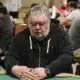 mies istuu pokeripöydässsä. Hänellä on päällään tumma huppari. Miehellä on kädet pöydällä ja hän peittää pelikortit.
