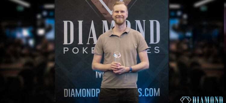Mies seisoo palkinto kädessään. Hän hymyilee ja hänellä on päällään vaaleanruskea t-paita.Takana näkyy Diamond Poker Serieksen kyltti.
