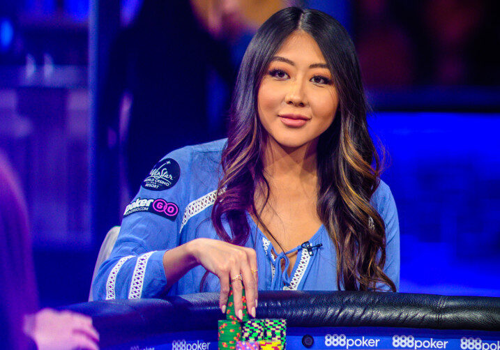 Tummahiuksinen nainen istuu pokeripöydässä ja koskee pelimerkkeihin. Tausta on sinertävä.