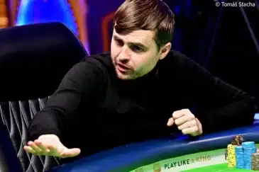 Kuvassa on intensiivinen hetki pokeriturnauksen pelipöydästä. Mustaan poolopaitaan pukeutunut pelaaja nojaa eteenpäin ja näyttää reagoivan voimakkaasti pelin tapahtumiin, joko puhumalla tai elehtimällä. Hänen kätensä on ojennettuna pöydän ylle, mikä lisää hetken dynaamisuutta. Pelaajan ilme on erittäin keskittynyt ja latautunut. Pöydällä hänen edessään on pinoja sinisiä ja keltaisia pelimerkkejä. Taustan epätarkat valot luovat ammattimaisen ja jännittyneen tunnelman. Valokuvaaja Tomáš Stacha on vanginnut hetken, joka on täynnä pokerin psykologista draamaa.