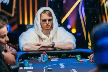 Ossi Ketola istuu poekripöydässä valkoisessa karvahupparissa aurinkolasit silmillään ja kädet ristissä