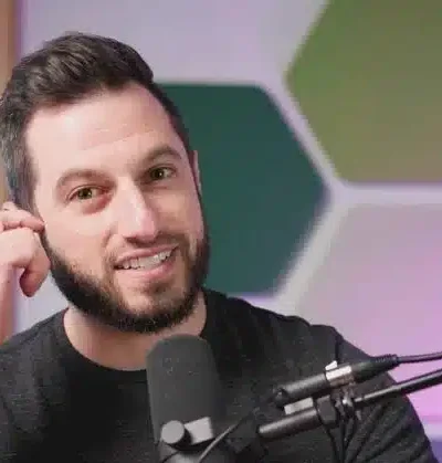 Kuvassa tummahiuksinen mies koskee korvaansa ja hänen edessään on mikrofoni. Tausta on värikäs.