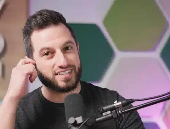 Kuvassa tummahiuksinen mies koskee korvaansa ja hänen edessään on mikrofoni. Tausta on värikäs.