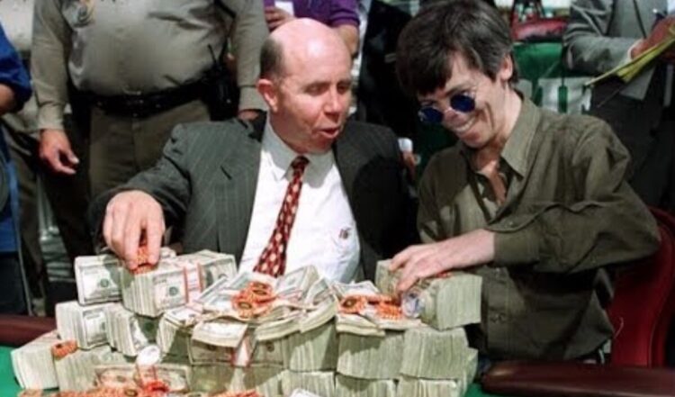 Kuvassa on ikoninen ja historiallinen hetki pokerimaailmasta. Siinä nähdään pokerilegenda Stu "The Kid" Ungar (oikealla) hänen voitettuaan World Series of Poker -pääturnauksen, todennäköisesti vuonna 1997. Ungar, jolla on tunnusomaiset pyöreät aurinkolasit, hymyilee leveästi. Hänen vieressään kasinojohtaja Jack Binion esittelee vaikuttavaa näkyä: vihreä pelipöytä on peitetty valtavalla määrällä käteistä rahaa, joka on pinottu korkeiksi nupuiksi, sekä tuhansilla pokerimerkeillä. Tämä oli perinteinen tapa esitellä turnauksen miljoonan dollarin pääpalkintoa. Kuva vangitsee täydellisesti vanhan ajan Las Vegasin tunnelman ja valtavan voiton suuruuden.