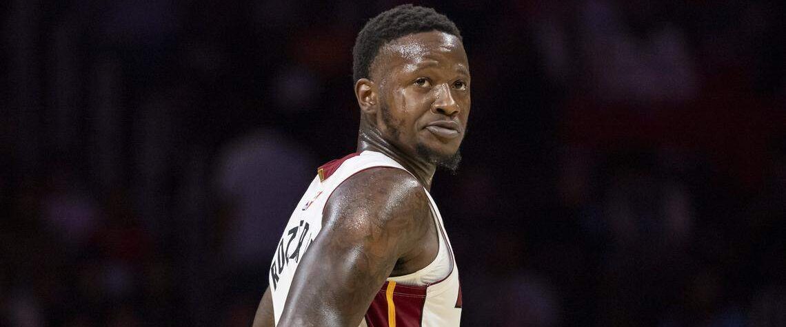 Kuvassa on koripalloilija Terry Rozier kesken Miami Heat -ottelun. Hän seisoo kentällä hieman sivuttain, mutta kääntää päätään ja katsoo taakseen olkansa yli intensiivisellä ja keskittyneellä ilmeellä. Rozierilla on yllään Heatin valkoinen pelipaita, jossa on punakeltaiset yksityiskohdat, ja hänen tatuoidut käsivartensa ovat selvästi näkyvissä. Kuvan tausta on sumennettu, mikä korostaa pelaajaa ja vangitsee pelin keskittyneen hetken.