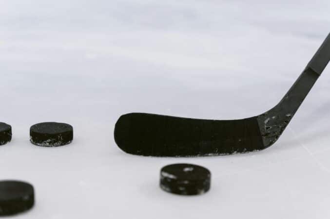 Jäällä jääkiekkomailan lapa ja neljä kiekkoa eri etäisyyksillä jääkiekkomailasta