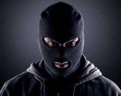 Kuvassa on lähikuva henkilöstä, jolla on yllään musta kommandopipo (balaclava), joka peittää kasvot lukuun ottamatta silmiä ja suuta. Henkilöllä on myös tumma huppari. Hänet on valaistu voimakkaasti suoraan edestä, mikä jättää taustan tummaksi ja luo dramaattisen varjon hänen ympärilleen. Henkilön katse on tuima ja tuijottaa suoraan kameraan. Kuva luo tarkoituksellisesti salamyhkäisen ja uhkaavan tunnelman.