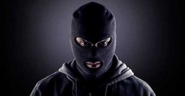 Kuvassa on lähikuva henkilöstä, jolla on yllään musta kommandopipo (balaclava), joka peittää kasvot lukuun ottamatta silmiä ja suuta. Henkilöllä on myös tumma huppari. Hänet on valaistu voimakkaasti suoraan edestä, mikä jättää taustan tummaksi ja luo dramaattisen varjon hänen ympärilleen. Henkilön katse on tuima ja tuijottaa suoraan kameraan. Kuva luo tarkoituksellisesti salamyhkäisen ja uhkaavan tunnelman.