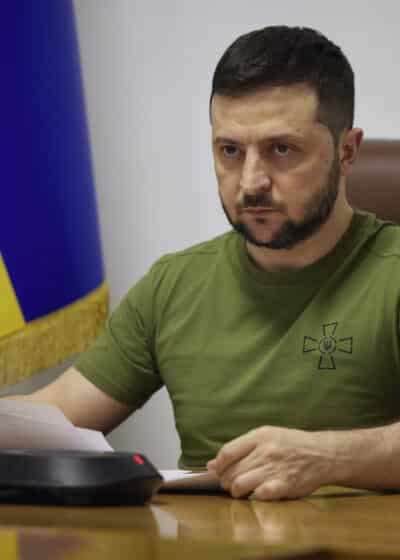 Ukrainan presidentti Zelenskyi istuu puupöydän ääressä edessään papereita ja taustalla Ukrainan lippu