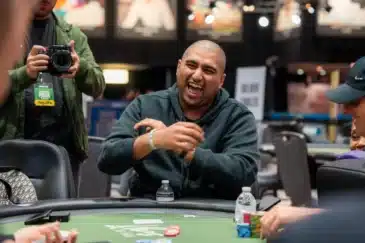 Nik Airball istuu pokeripöydän ääressä naureskellen leveästi. Häntä kuvaa kameralla vieressä mies.