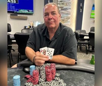 Mies istuu pokeripöydässä. Hänellä on kädessään kaksi pelikorttia. Miehen edessä pöydällä on iso suuri kasa pelimerkkejä.