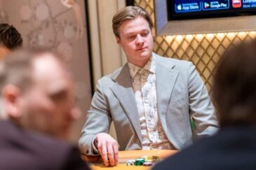 Casimir Seire istuu pokeripöydässä. Hänellä on päällään harmaa puku, jonka alla vaalea kauluspaita. Tausta on kultaista ja ruskeaa.